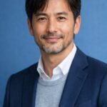 清潔感のある40代・50代の日本人男性が青い背景の前でやさしく微笑む、爪ケア記事向けの上半身ポートレート画像