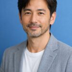 清潔感のある40代・50代の日本人男性が、青系の無地背景の前でやさしく微笑む上半身ポートレート。自然光のような柔らかい光で、健康的で落ち着いた印象の広告用アイキャッチ画像。