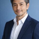 清潔感のある40代〜50代日本人男性の上半身ポートレート、青背景で自然光の爽やかな印象