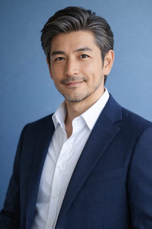 清潔感のある40代〜50代日本人男性の上半身ポートレート、青背景で自然光の爽やかな印象