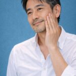 春の青基調背景の中で頬に手を当てる清潔感のある40代日本人男性