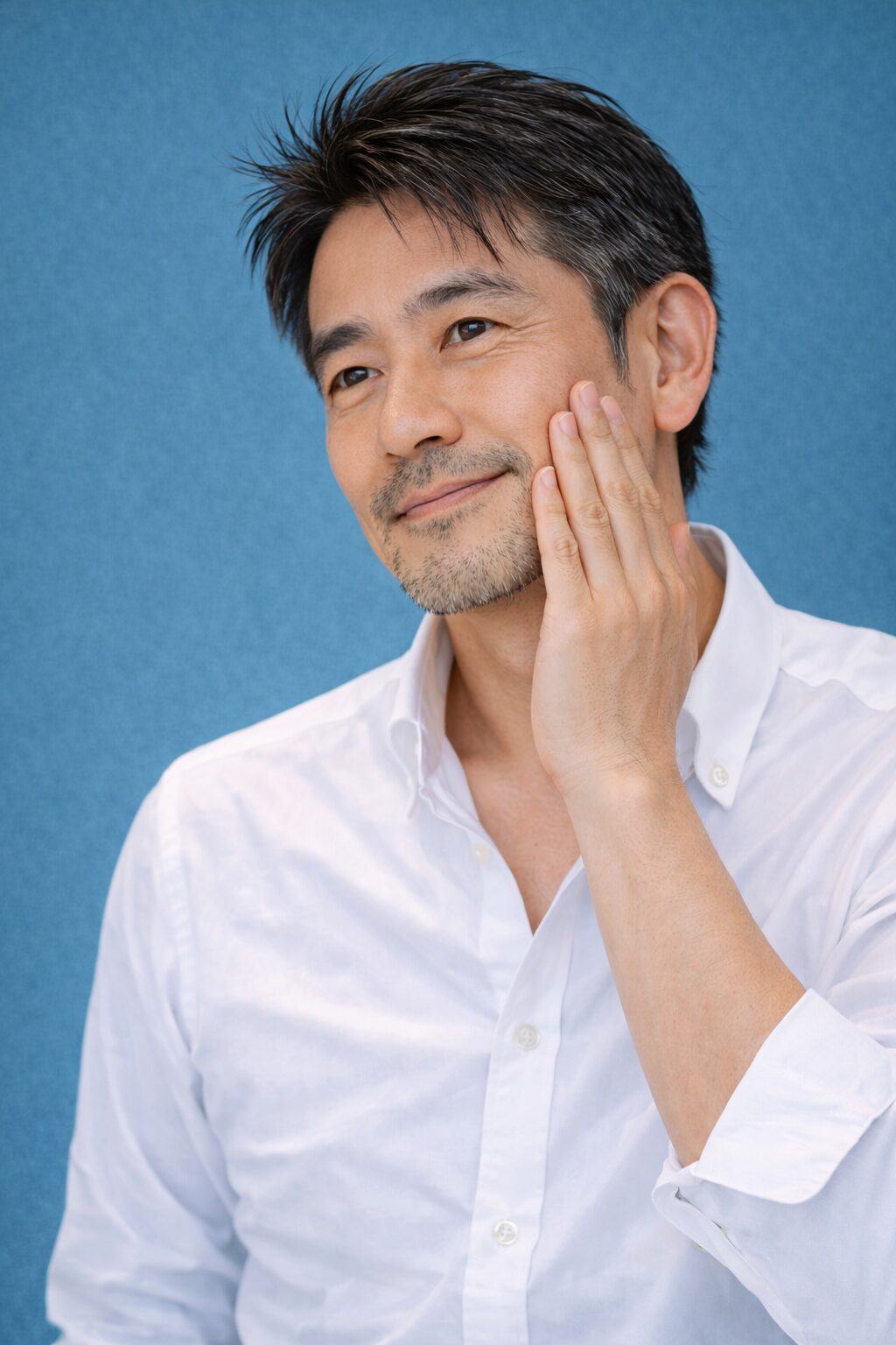 春の青基調背景の中で頬に手を当てる清潔感のある40代日本人男性